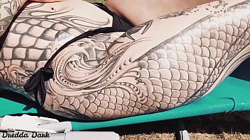 Tattooed horny brunette with big boobs sunbathing in the yard and rubbing sunscreen on her tits