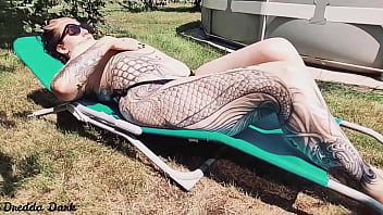 Tattooed horny brunette with big boobs sunbathing in the yard and rubbing sunscreen on her tits