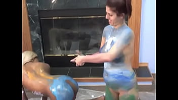 Two lesbians smear each other with paints for drawing on the floor near the fireplace