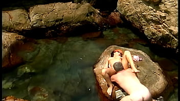 A mature man fucks an exotic babe wearing only a cap and sunglasses on the seaside stones
