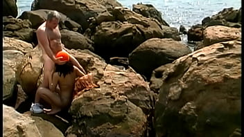 A mature man fucks an exotic babe wearing only a cap and sunglasses on the seaside stones