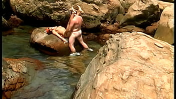 A mature man fucks an exotic babe wearing only a cap and sunglasses on the seaside stones