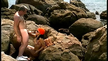 A mature man fucks an exotic babe wearing only a cap and sunglasses on the seaside stones